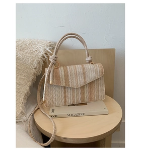 Detail of a woven straw handbag with beige stripes and decorative knotted handle on a desk