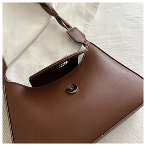 Detail of dark brown leather underarm bag with unique woven strap and metal magnetic closure