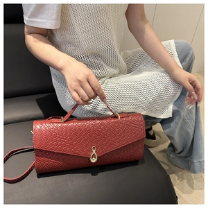 Dettaglio di pochette rosso vino in pelle intrecciata con chiusura dorata e tracolla