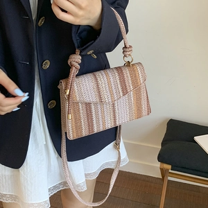 Close-up of a striped woven crossbody bag with envelope flap on a fashion model