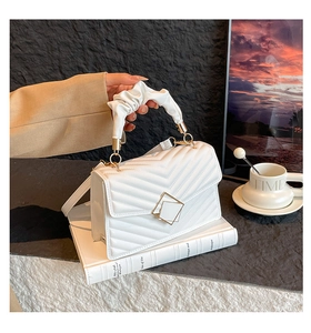 Detail of white quilted bag with V-shaped texture, cloud handle and gold geometric lock