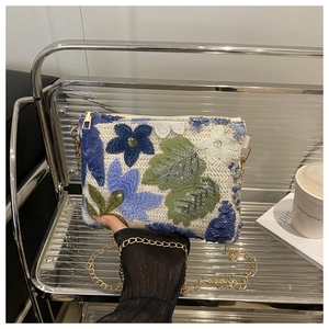 Détail de broderie florale à paillettes sur pochette beige avec chaîne dorée