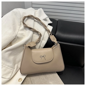 Detail of the woven rope shoulder strap and gold metal bow clasp on a beige leather bag