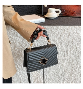 Close-up of black quilted shoulder bag with golden buckle and ruched handle detail