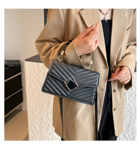 Detail view of black quilted crossbody bag with golden square lock and leather handle