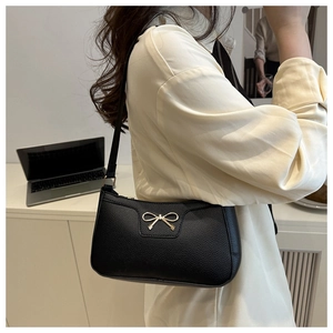Detail of black pebbled leather underarm bag with a golden metal bow decoration