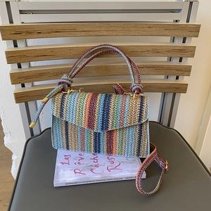 Detail of colorful striped woven shoulder bag on vintage book and wooden backdrop