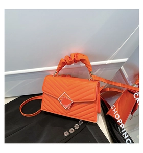 Detail of orange quilted crossbody bag featuring metal buckle and ruched handle