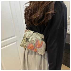 Détail de pochette à paillettes avec broderie florale orange et fine chaîne dorée