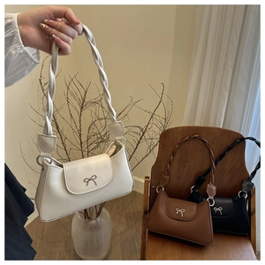 Detailed view of woven shoulder straps and silver bow charms on minimalist handbags