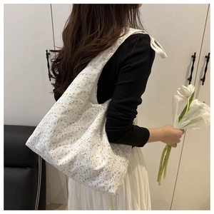 Détail d'un sac cabas en dentelle blanche avec motifs floraux jaunes porté par un mannequin