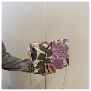 Détail de broderie florale en paillettes mauves et chaîne dorée sur pochette beige