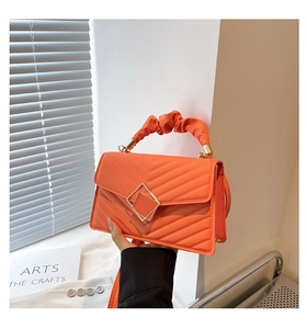 Detail of orange quilted leather bag featuring a pleated handle and square metal buckle