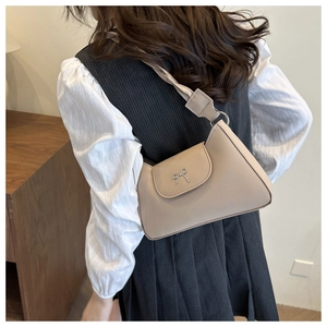 Detail of light beige underarm bag featuring a metallic silver bow and curved bottom