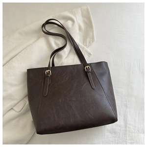 Dettaglio borsa tote in pelle marrone scuro con fibbie dorate su camicia di velluto bianco