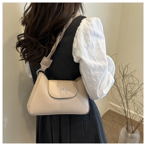 Detail of beige shoulder bag featuring metal bow ornament and twisted braided strap