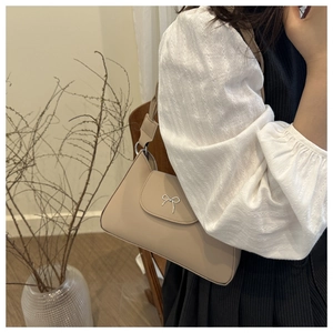 Chic beige underarm bag with metal bow detail shown on a model in a cozy room