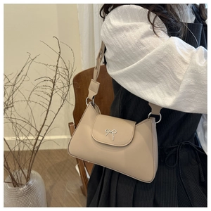 Close-up of beige leather shoulder bag featuring a decorative silver bow buckle and strap