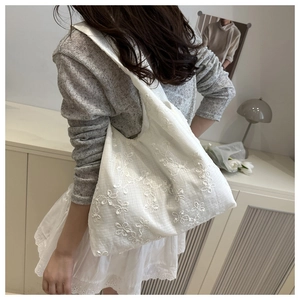 Lace flower embroidered white canvas tote bag shown styled on shoulder in minimalist home