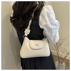 Close-up of cream leather shoulder bag featuring a silver bow detail and wide strap
