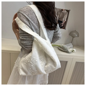 Détail de la broderie florale blanche sur un sac fourre-tout porté par un mannequin