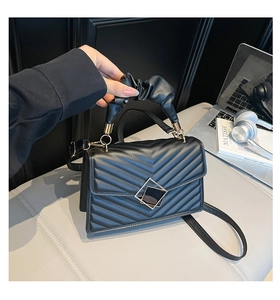 Detail of a black quilted bag with golden square clasp and pleated top handle