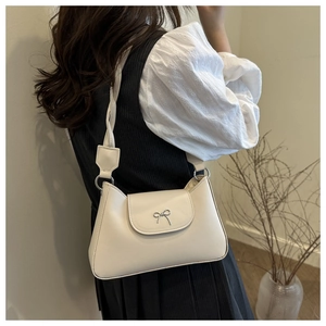 Detail of a beige underarm bag with a silver metal bow and braided shoulder strap