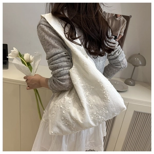 Détail de la broderie florale sur un sac cabas en toile blanche au tissu texturé