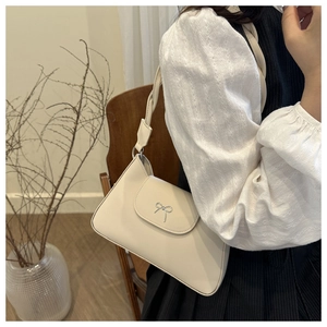 Close-up of off-white underarm bag with silver bow buckle against a warm indoor background