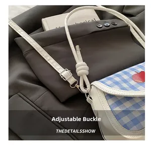 Détail de la boucle argentée ajustable et de la bandoulière en cuir blanc du sac à carreaux