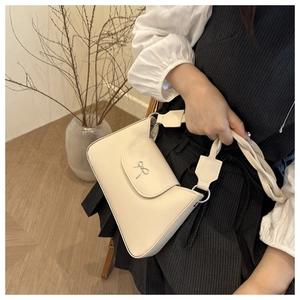 Detail of cream white leather shoulder bag featuring a silver metal 3D bow buckle