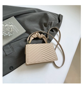 Detail of beige quilted faux leather bag with pleated handle and golden hardware