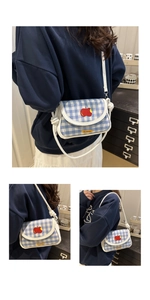 Détail du sac à carreaux bleus et blancs avec broderie pomme rouge et bandoulière blanche