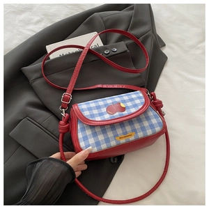 Détail du sac bandoulière en cuir rouge avec rabat à carreaux bleus et patch pomme