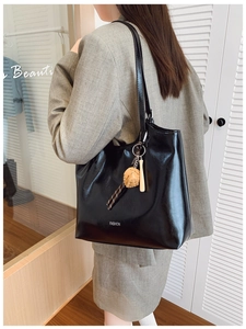 Detail of black glossy tote bag featuring a baseball charm and white fashion lettering