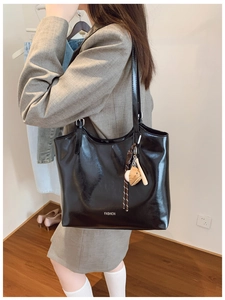 Detail of glossy black tote bag with fashion text and baseball charm pendant