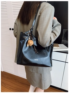 Detail of a large black glossy tote bag with FASHION logo and a brown charm pendant