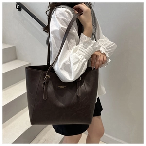 Detail of dark brown leather tote bag showing shoulder strap buckles and brand patch