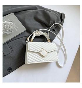 Close-up of white quilted handbag featuring a golden geometric buckle and ruched handle