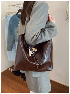 Close-up of brown glossy tote bag with fashion lettering and baseball pendant detail