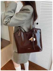 Detail of a dark brown glossy tote bag with FASHION text and a mini baseball charm