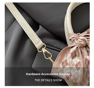 Close-up of golden hardware hook and pink lattice silk scarf on a white leather handbag