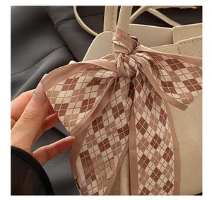 Close-up of beige leather handbag handle featuring a decorative plaid bow scarf detail