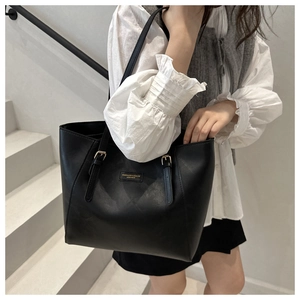 Detailaufnahme einer schwarzen Leder-Shopper-Tasche mit verstellbaren Trägern und Goldplakette