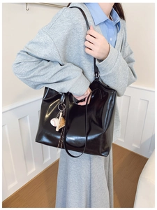 Detailed view of black patent leather tote bag with FASHION logo and baseball charm