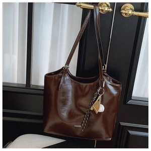 Detail of dark brown leather tote bag with FASHION logo and sports-themed charm