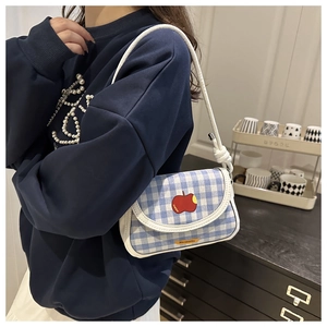 Détail du sac à carreaux bleus avec broderie pomme rouge porté par un modèle