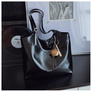 Detail of glossy black tote bag featuring a baseball charm and silver FASHION logo