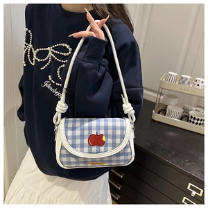 Détail du sac selle à carreaux bleus avec broderie pomme rouge et passepoil en cuir blanc