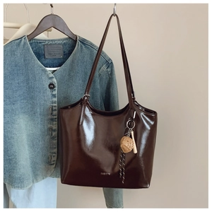 Close-up of glossy brown tote bag with silver FASHION logo and decorative ball pendant